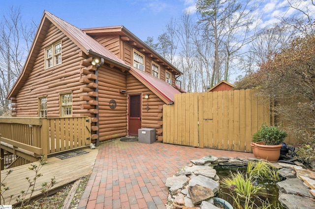 rear view of house with a deck, a patio, fence, metal roof, and log exterior