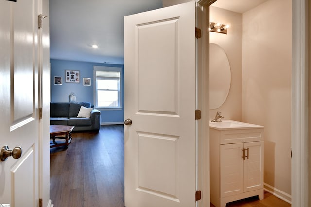 hall with a sink, baseboards, and dark wood-type flooring