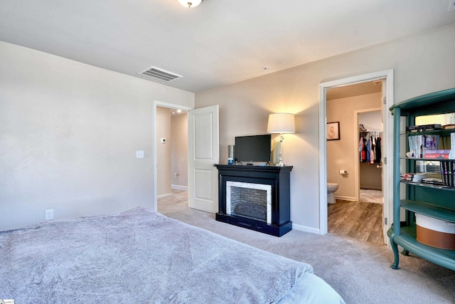 carpeted bedroom with visible vents, baseboards, ensuite bathroom, and a fireplace