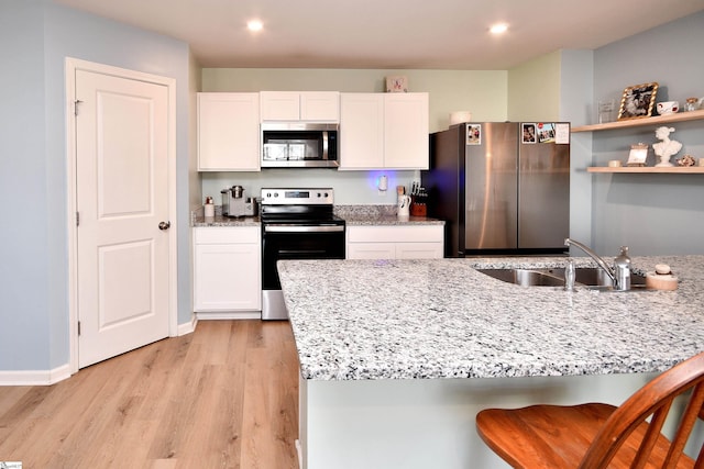 kitchen featuring light wood-type flooring, a sink, stainless steel appliances, white cabinets, and light stone countertops