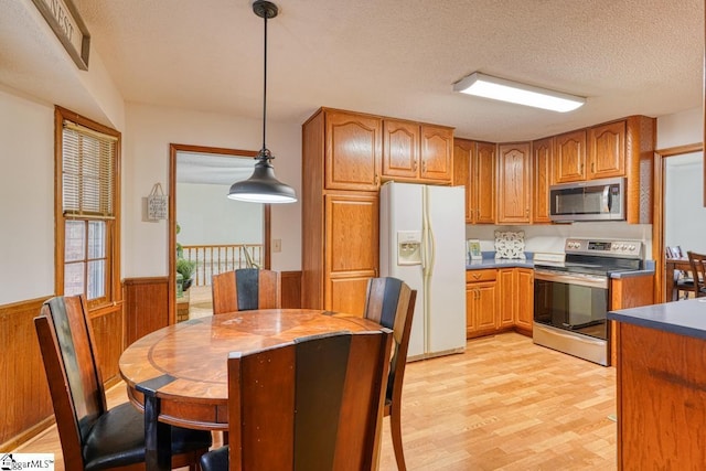 kitchen featuring wooden walls, a wainscoted wall, stainless steel appliances, a textured ceiling, and brown cabinets