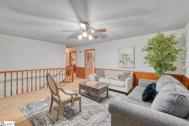 carpeted living room featuring a wainscoted wall, a textured ceiling, wood walls, and a ceiling fan