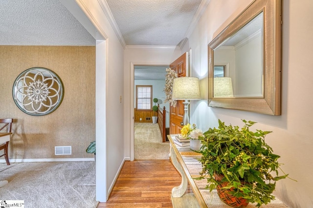 hall featuring visible vents, a textured ceiling, crown molding, wallpapered walls, and baseboards