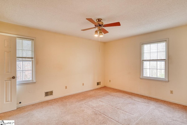 empty room with visible vents, light carpet, a healthy amount of sunlight, and ceiling fan