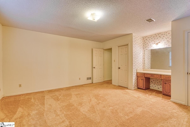 unfurnished bedroom featuring baseboards, visible vents, wallpapered walls, a textured ceiling, and light colored carpet