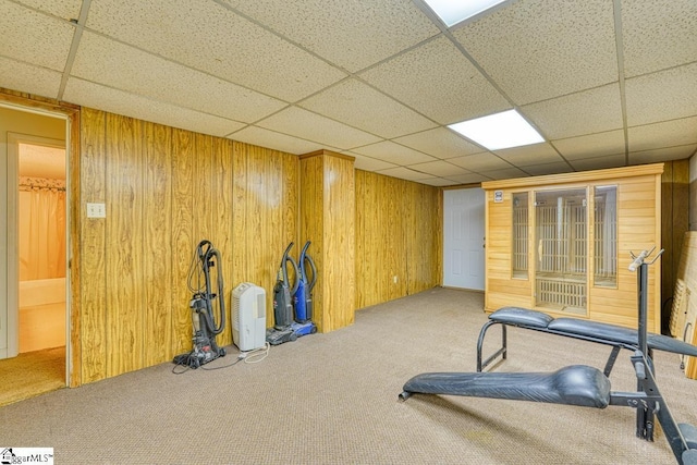 exercise area featuring wooden walls, carpet flooring, and a drop ceiling