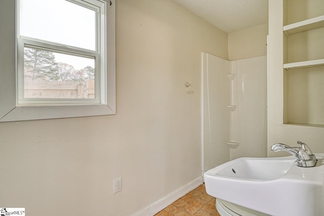 bathroom with tile patterned flooring, walk in shower, baseboards, and a sink