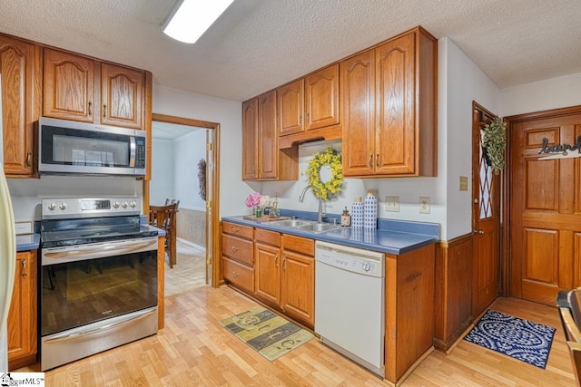 kitchen with a sink, brown cabinetry, light wood finished floors, and stainless steel appliances