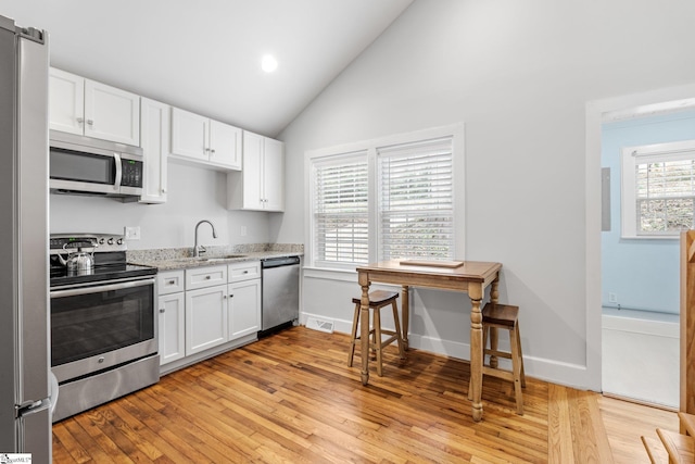 kitchen featuring vaulted ceiling, white cabinets, stainless steel appliances, and a sink