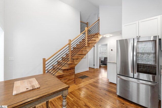 interior space featuring visible vents, smart refrigerator, white cabinetry, wood-type flooring, and a high ceiling