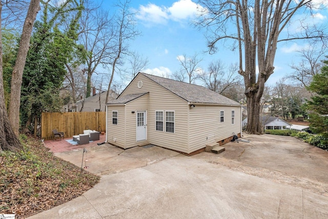 rear view of house with a shingled roof, fence, entry steps, concrete driveway, and a patio