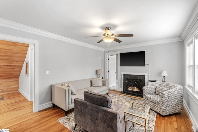 living room with light wood-type flooring, a fireplace with flush hearth, visible vents, ornamental molding, and a ceiling fan