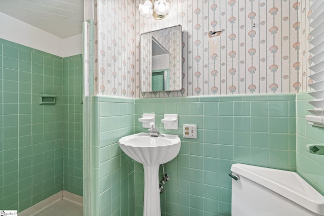 bathroom featuring wallpapered walls, tile walls, toilet, and wainscoting