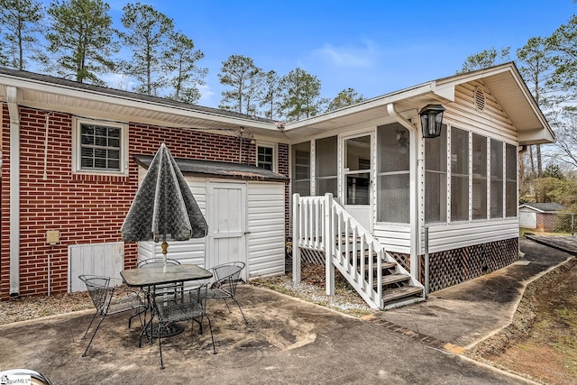 back of property with outdoor dining area, a sunroom, an outdoor structure, a patio area, and brick siding