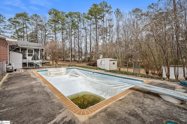 view of swimming pool with an outbuilding, a shed, a sunroom, a diving board, and a patio area