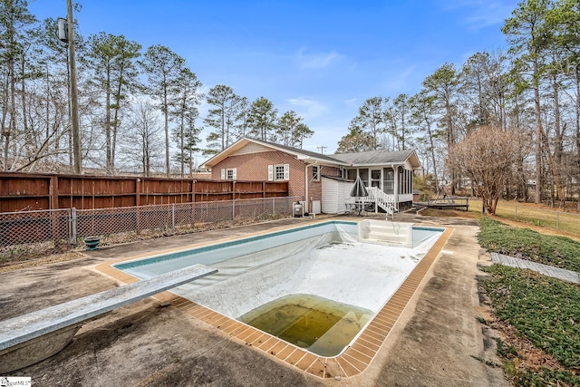 view of swimming pool featuring a fenced backyard, a sunroom, a diving board, a fenced in pool, and a patio area