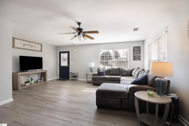 living room featuring visible vents, baseboards, a ceiling fan, and wood finished floors