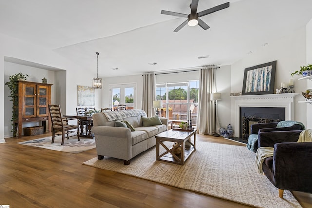 living area with wood finished floors, visible vents, a fireplace, vaulted ceiling, and ceiling fan with notable chandelier