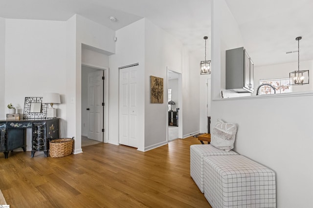 hall with wood finished floors, baseboards, visible vents, a towering ceiling, and a chandelier