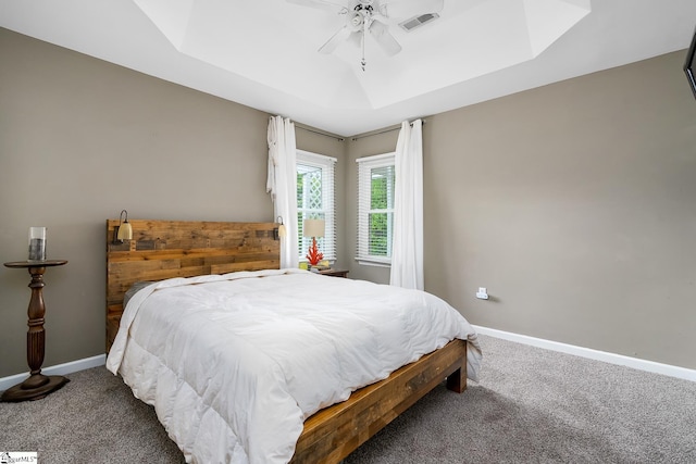 carpeted bedroom with visible vents, ceiling fan, baseboards, and a tray ceiling