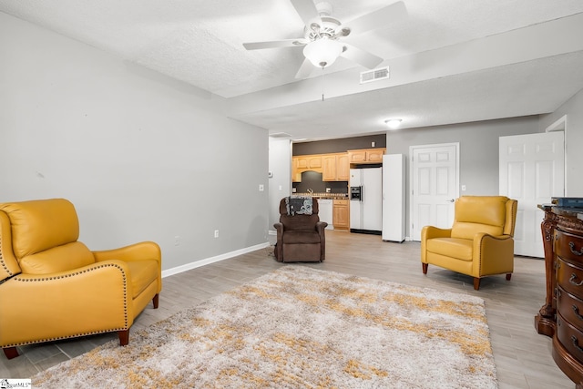 sitting room with a ceiling fan, visible vents, light wood finished floors, and a textured ceiling