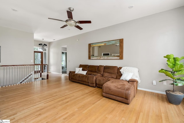 living room with ceiling fan with notable chandelier, wood finished floors, and baseboards