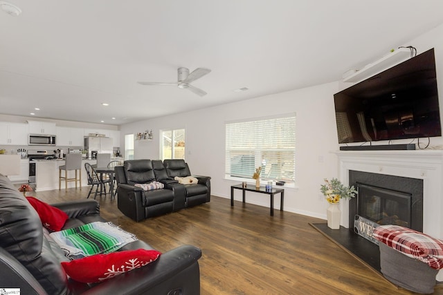 living area featuring dark wood-style floors, a ceiling fan, baseboards, recessed lighting, and a glass covered fireplace