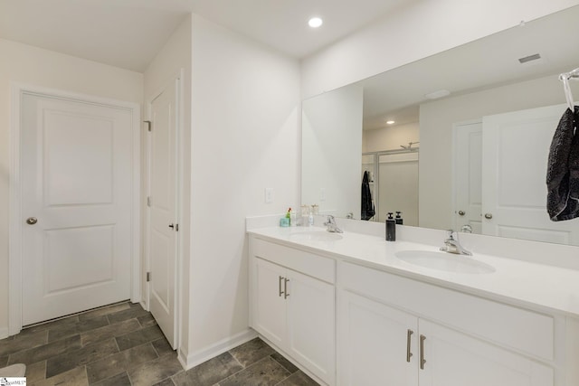 full bath featuring double vanity, stone finish floor, recessed lighting, and a sink