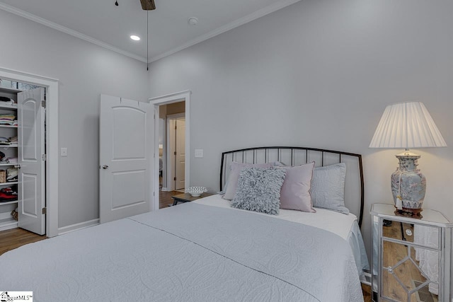 bedroom featuring a walk in closet, wood finished floors, recessed lighting, crown molding, and baseboards