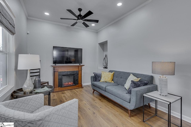 living area with baseboards, a premium fireplace, ornamental molding, wood finished floors, and a ceiling fan