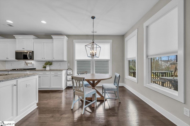 kitchen featuring stainless steel microwave, tasteful backsplash, white cabinetry, baseboards, and a chandelier