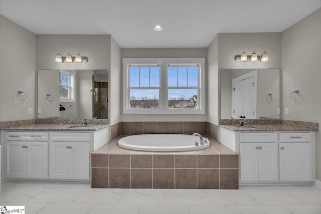 bathroom with a sink, marble finish floor, a garden tub, and two vanities