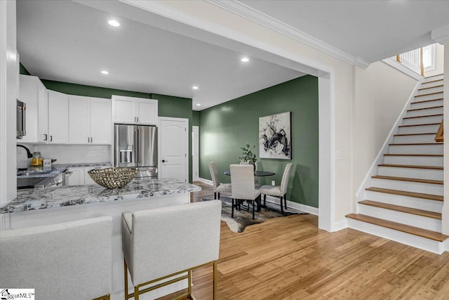 kitchen featuring light stone counters, white cabinetry, stainless steel fridge, light wood-style floors, and a peninsula