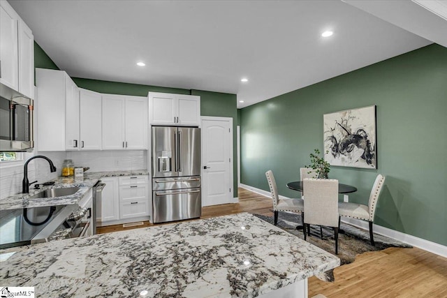 kitchen featuring white cabinetry, light wood-style flooring, light stone counters, and appliances with stainless steel finishes