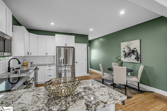 kitchen featuring light stone counters, white cabinets, light wood finished floors, and stainless steel appliances