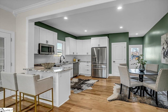 kitchen with light wood-style flooring, a sink, stainless steel appliances, a peninsula, and light stone countertops