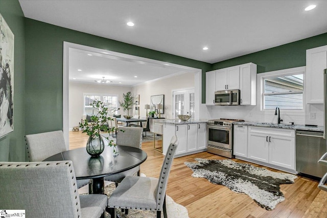 kitchen with a sink, light stone counters, light wood-style floors, appliances with stainless steel finishes, and white cabinets