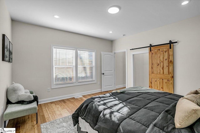 bedroom with a barn door, recessed lighting, light wood-style flooring, and baseboards