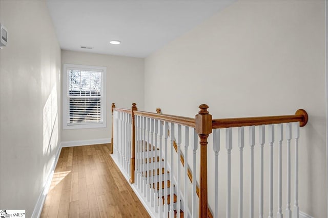 hall with light wood-type flooring, an upstairs landing, baseboards, and visible vents