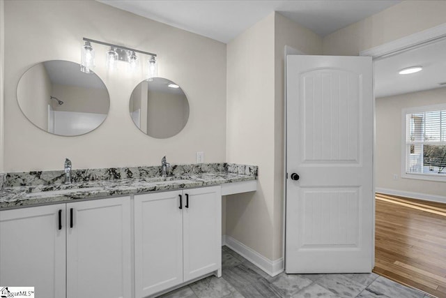 full bath with double vanity, wood finished floors, baseboards, and a sink