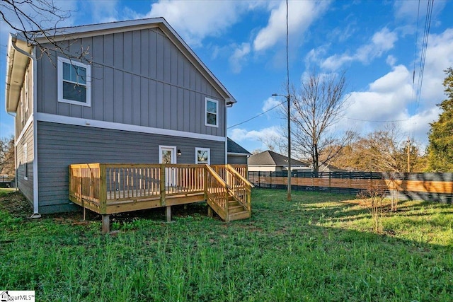 back of house with a lawn, board and batten siding, a deck, and fence