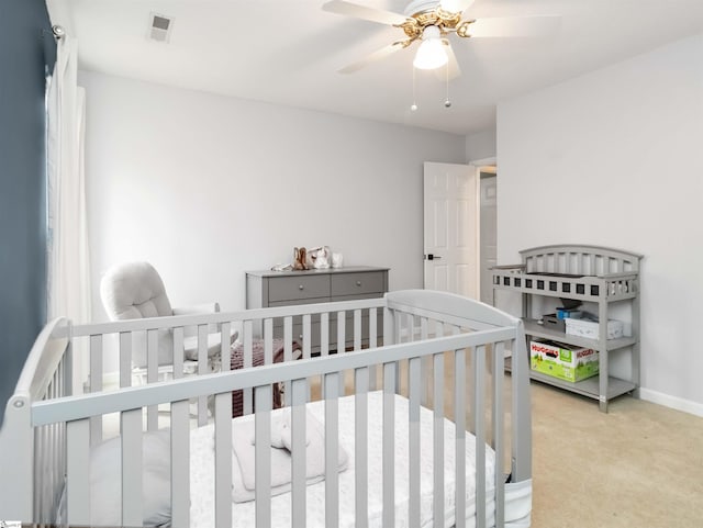 bedroom with visible vents, a nursery area, carpet, baseboards, and ceiling fan