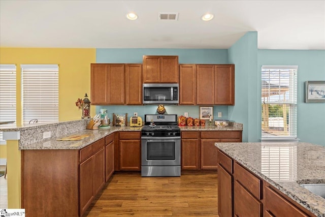 kitchen with visible vents, brown cabinets, wood finished floors, appliances with stainless steel finishes, and a peninsula