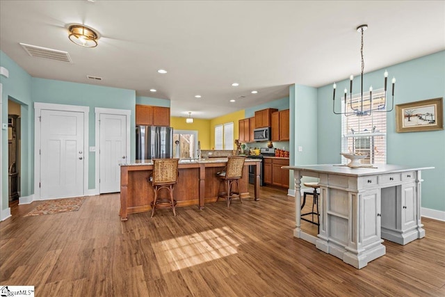 kitchen featuring brown cabinetry, visible vents, stainless steel appliances, and a kitchen island with sink