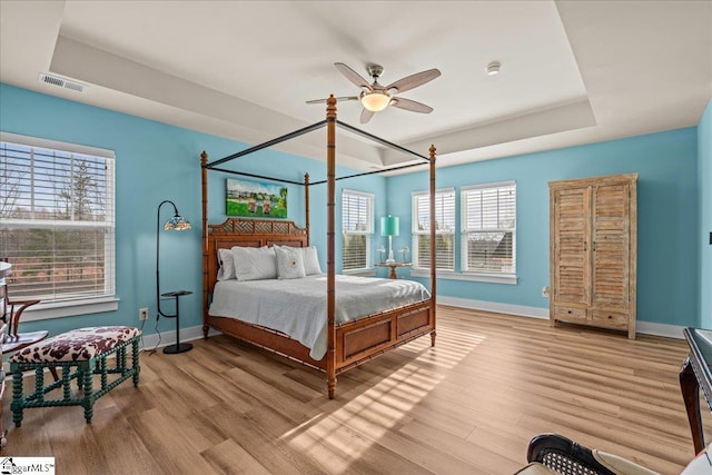 bedroom with a tray ceiling, wood finished floors, visible vents, and baseboards