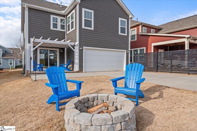 rear view of house with concrete driveway, an attached garage, and a fire pit