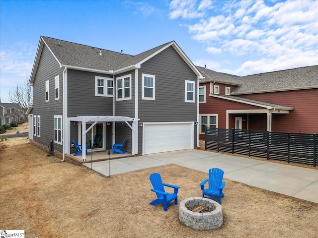 rear view of house featuring driveway, an outdoor fire pit, roof with shingles, an attached garage, and a patio area