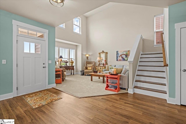 foyer entrance with stairway, baseboards, high vaulted ceiling, and wood finished floors