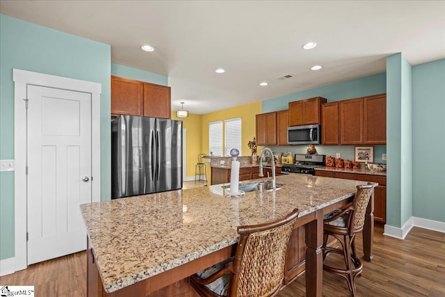 kitchen featuring a kitchen bar, visible vents, an island with sink, dark wood-style floors, and stainless steel appliances