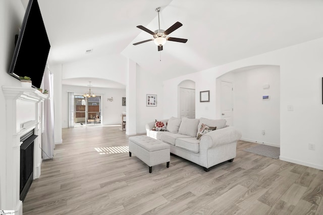 living area featuring arched walkways, light wood-style floors, a fireplace, and ceiling fan with notable chandelier